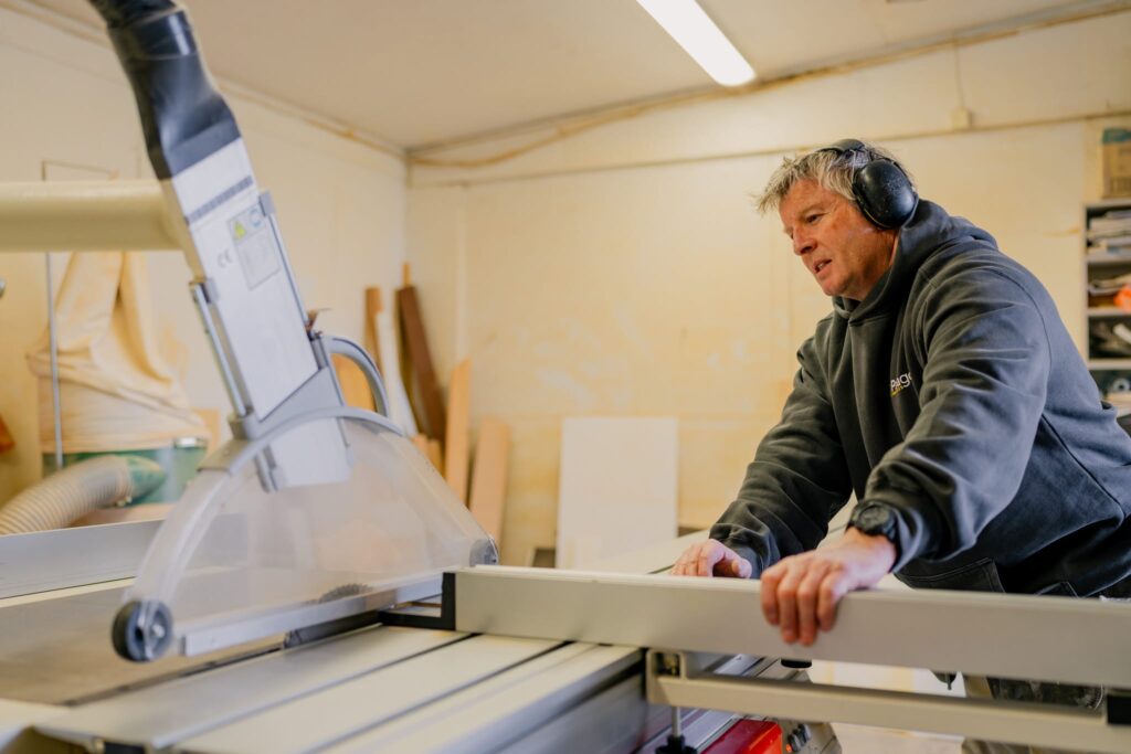 Builder operating saw in workshop constructing timber homes and new builds NZ, representing quality home builders and construction expertise in small homes New Zealand.