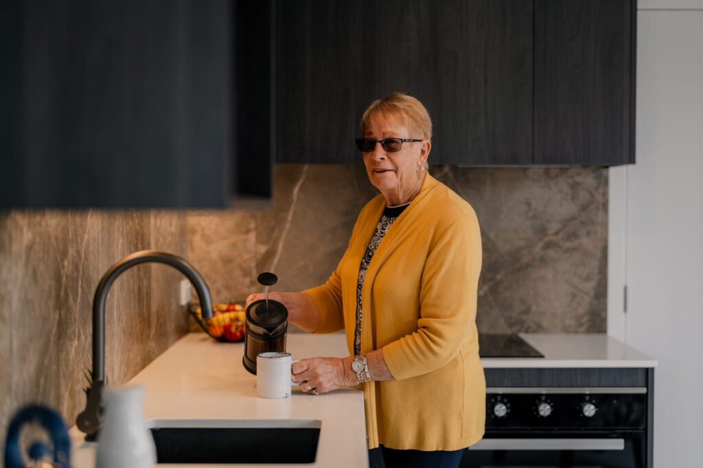 Senior woman preparing coffee inside modern kitchen of a small portable home NZ, showing premium design and easy build homes by New Zealand home builders.